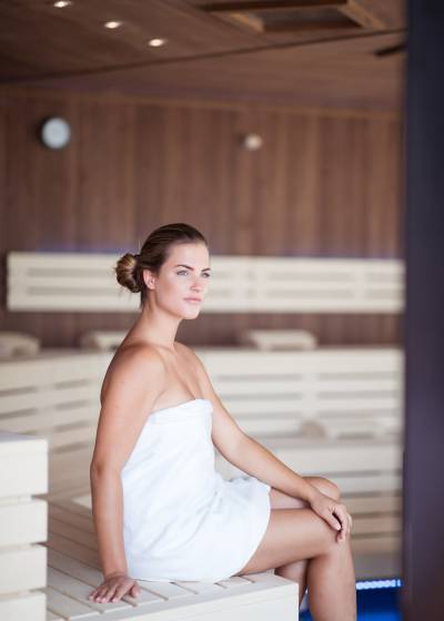 Frau sitzt mit Handtuch in der Sauna